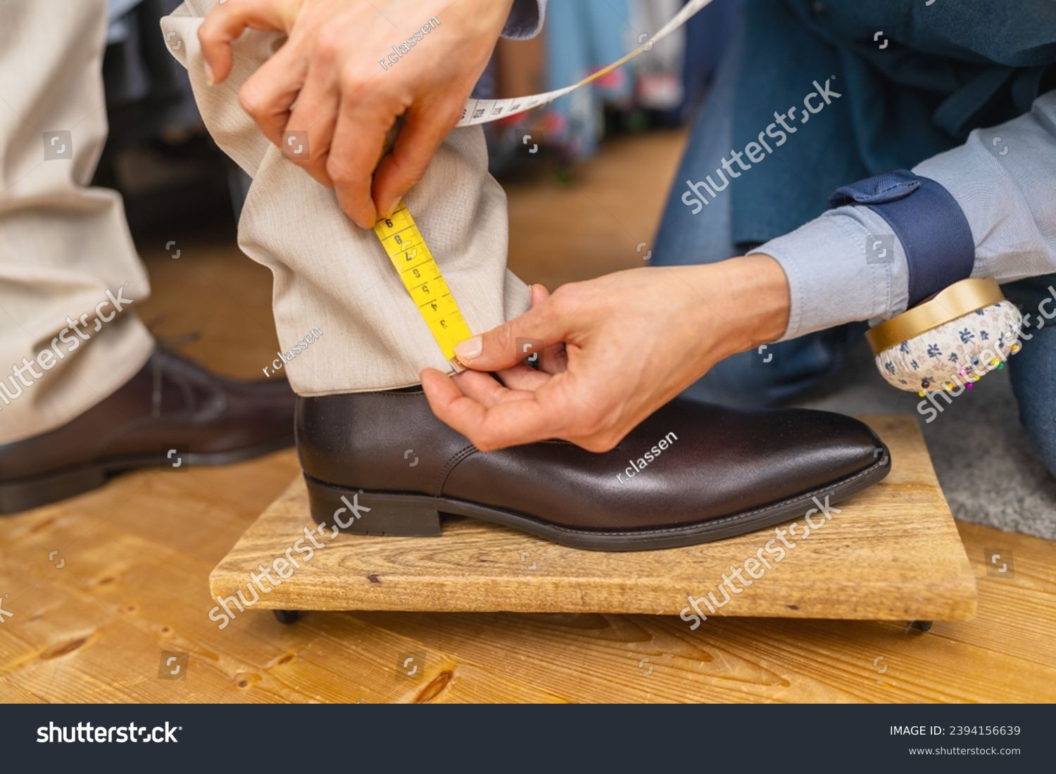 Measuring trouser length with tape on man's ankle above brown shoe #2394156639
