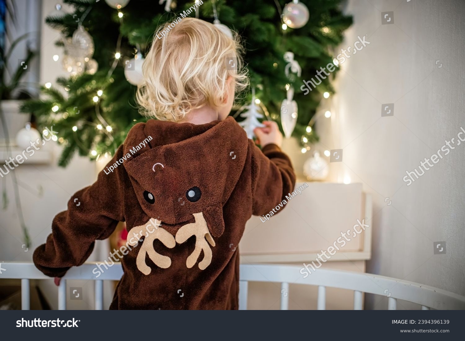 Little girl in reindeer costume decorating Christmas tree while standing in crib #2394396139