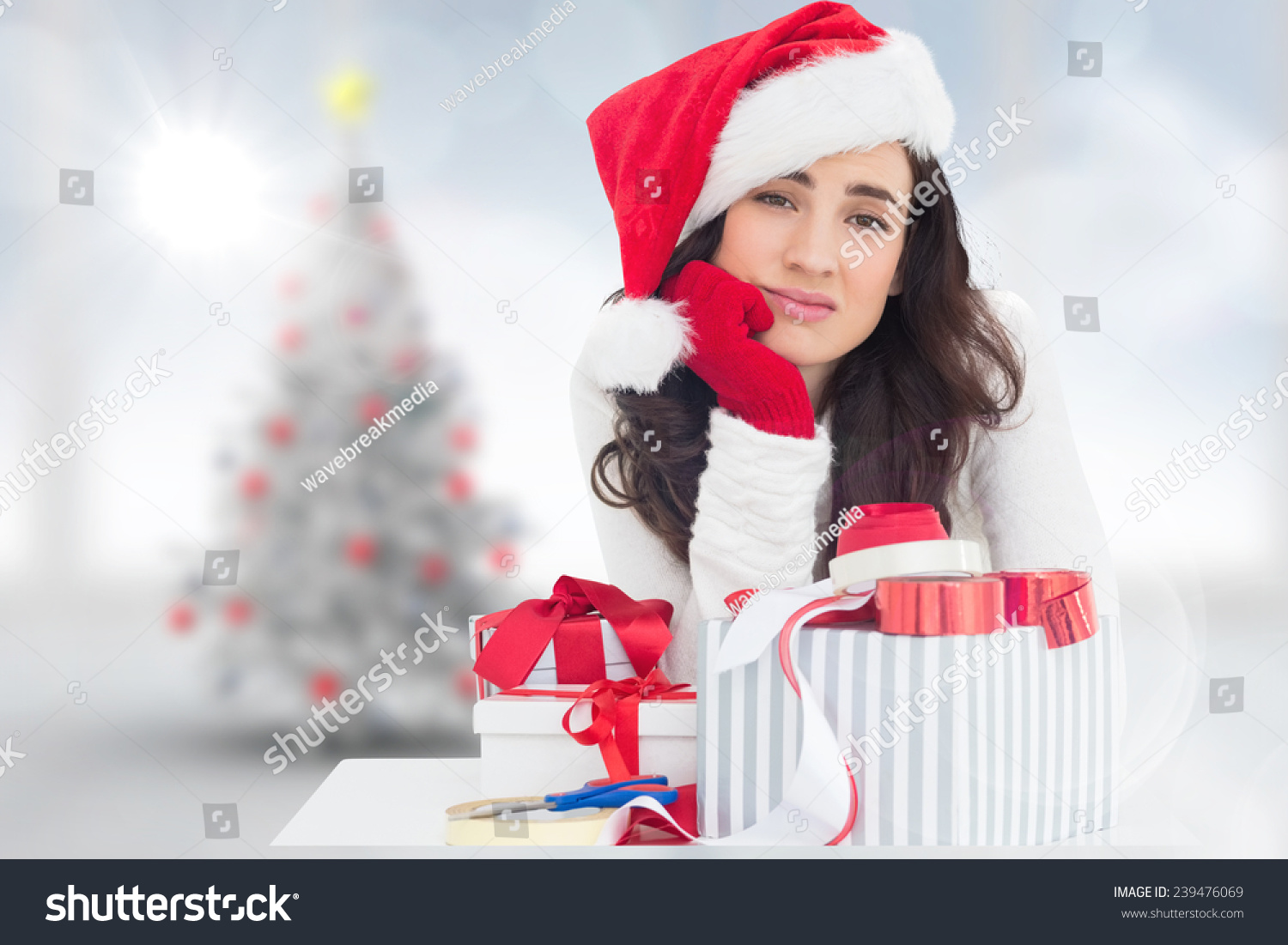 Unsure brunette in santa hat packing gifts against blurry christmas tree in room #239476069