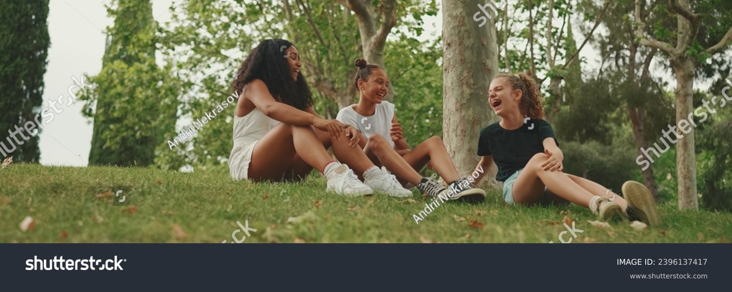 Three girls friends pre-teenage sit on the grass in the park and emotionally talking. Three teenagers on the outdoors #2396137417