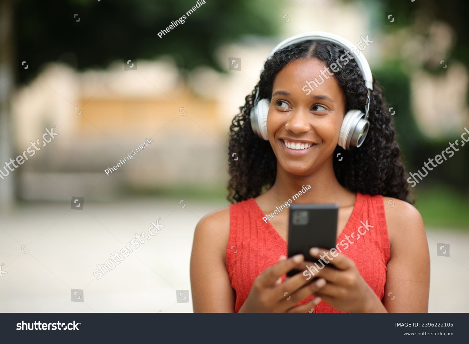 Front view portrait of a happy black woman looks at side listening to music walking in the street #2396222105