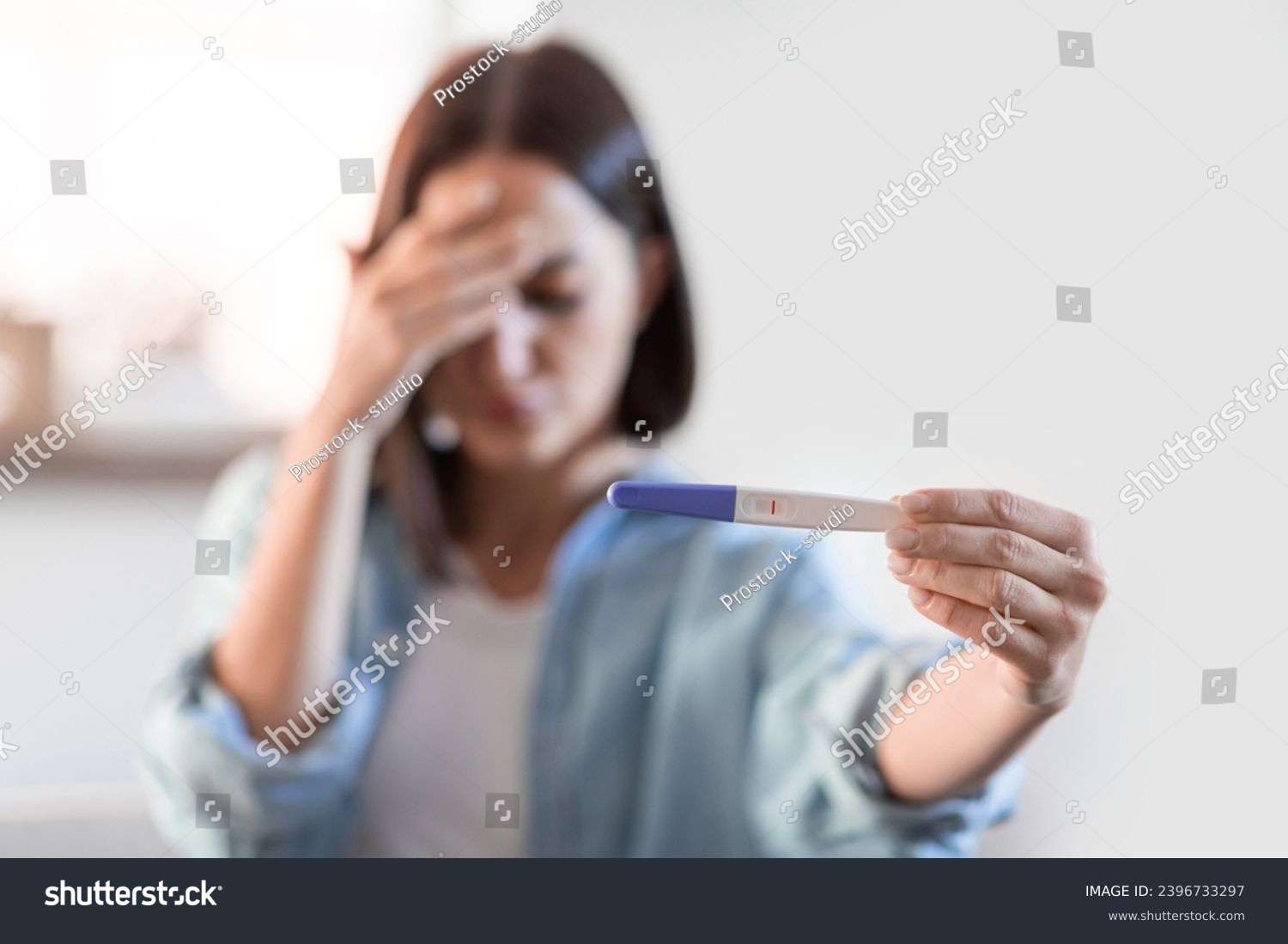 Infertility concept. Depressed unrecognizable lady showing negative pregnancy test at home interior. Selective focus on test result as depressed woman shows it to camera. Shallow depth #2396733297