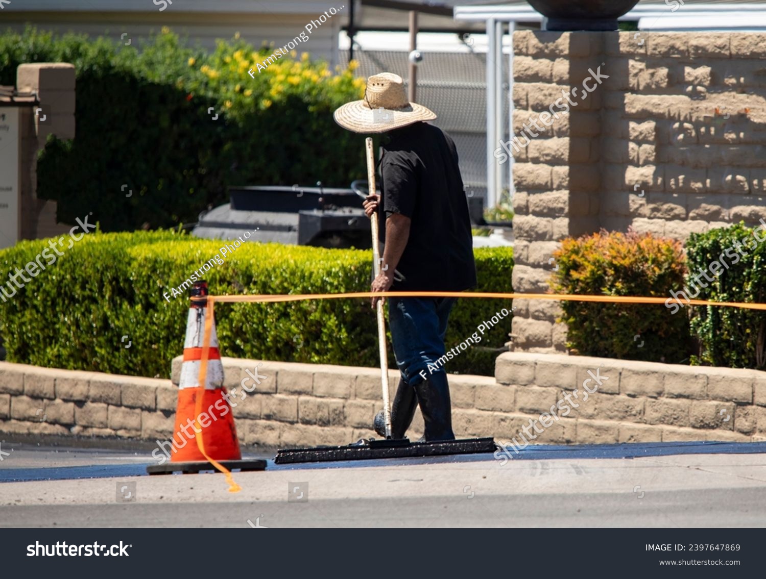 A man in a straw hat spreading new asphalt slurry  #2397647869