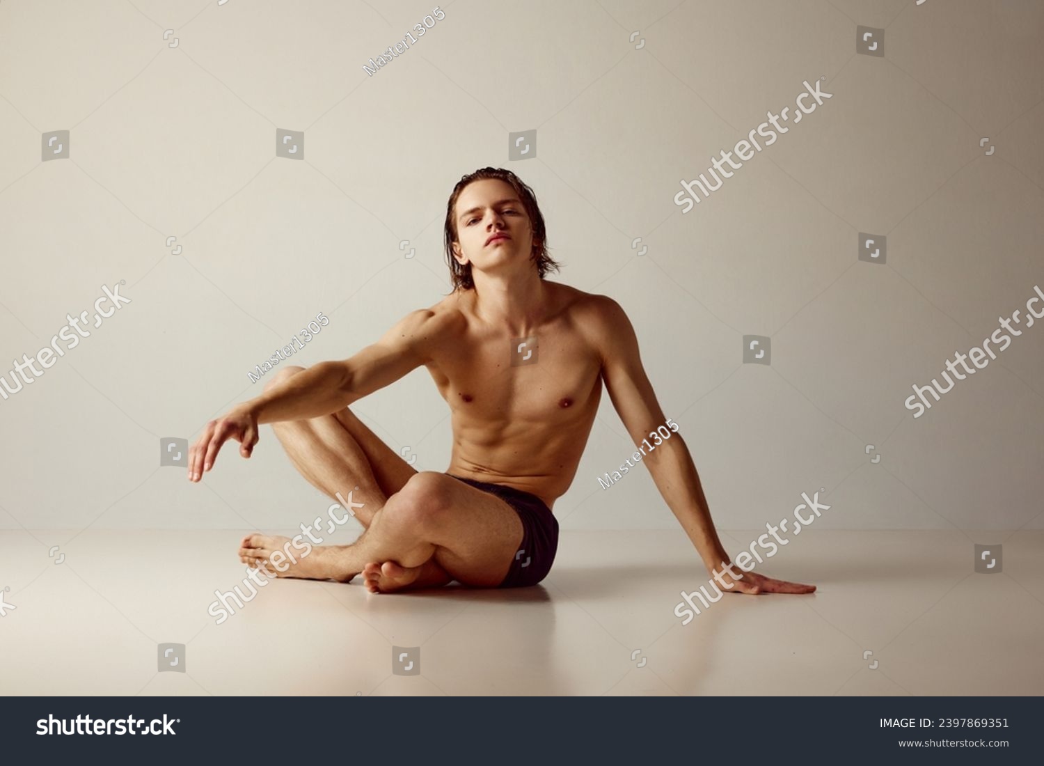 Handsome young guy with sportive, muscular body sitting on floor, posing shirtless in underwear against grey studio background. Concept of men's beauty, health, body care, sportive lifestyle #2397869351