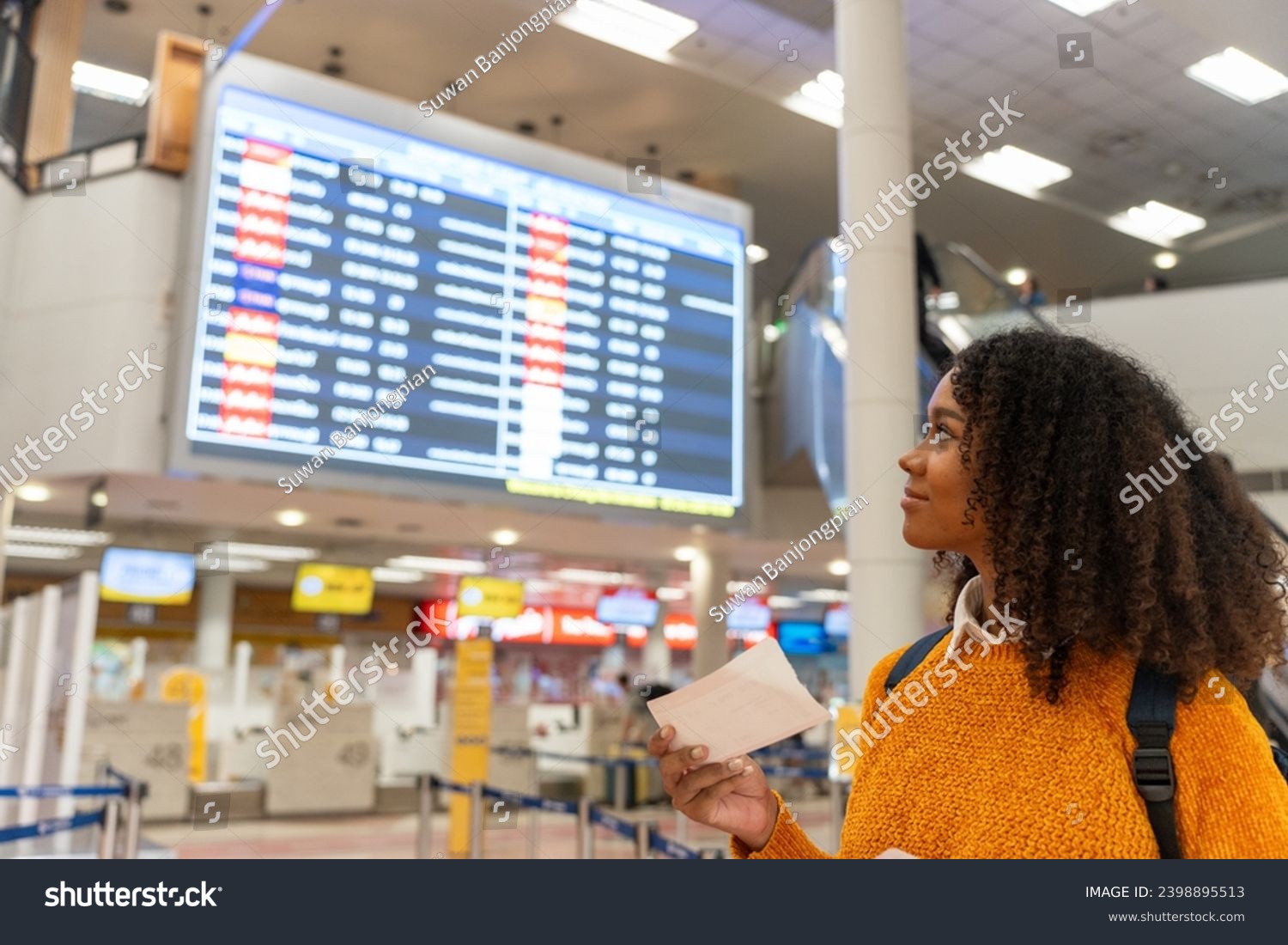 Black woman looks at the flight schedule on a digital monitor in an airport to check the gate and time to board the plane to travel or study abroad. #2398895513
