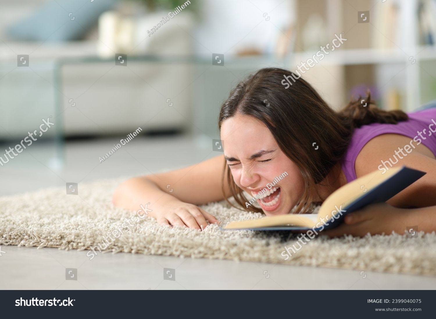 Happy woman lying on the floor laughing hilariously reading a book at home #2399040075