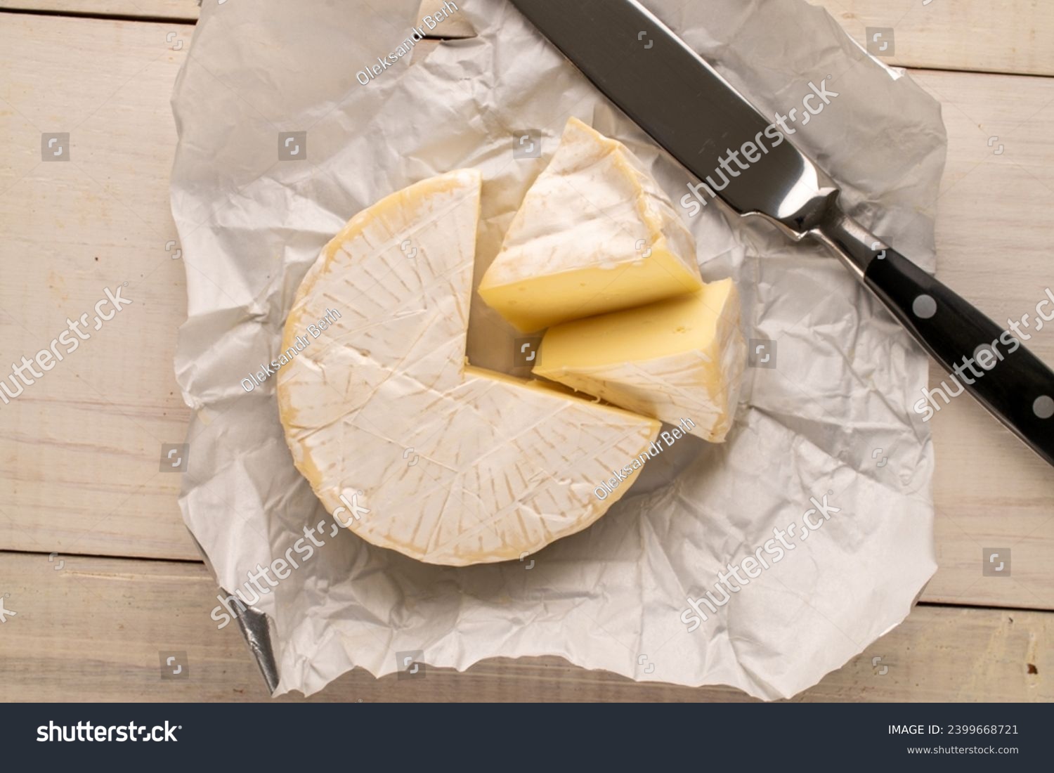 Fragrant brie cheese with paper package and knife on wooden table, macro, top view.

 #2399668721