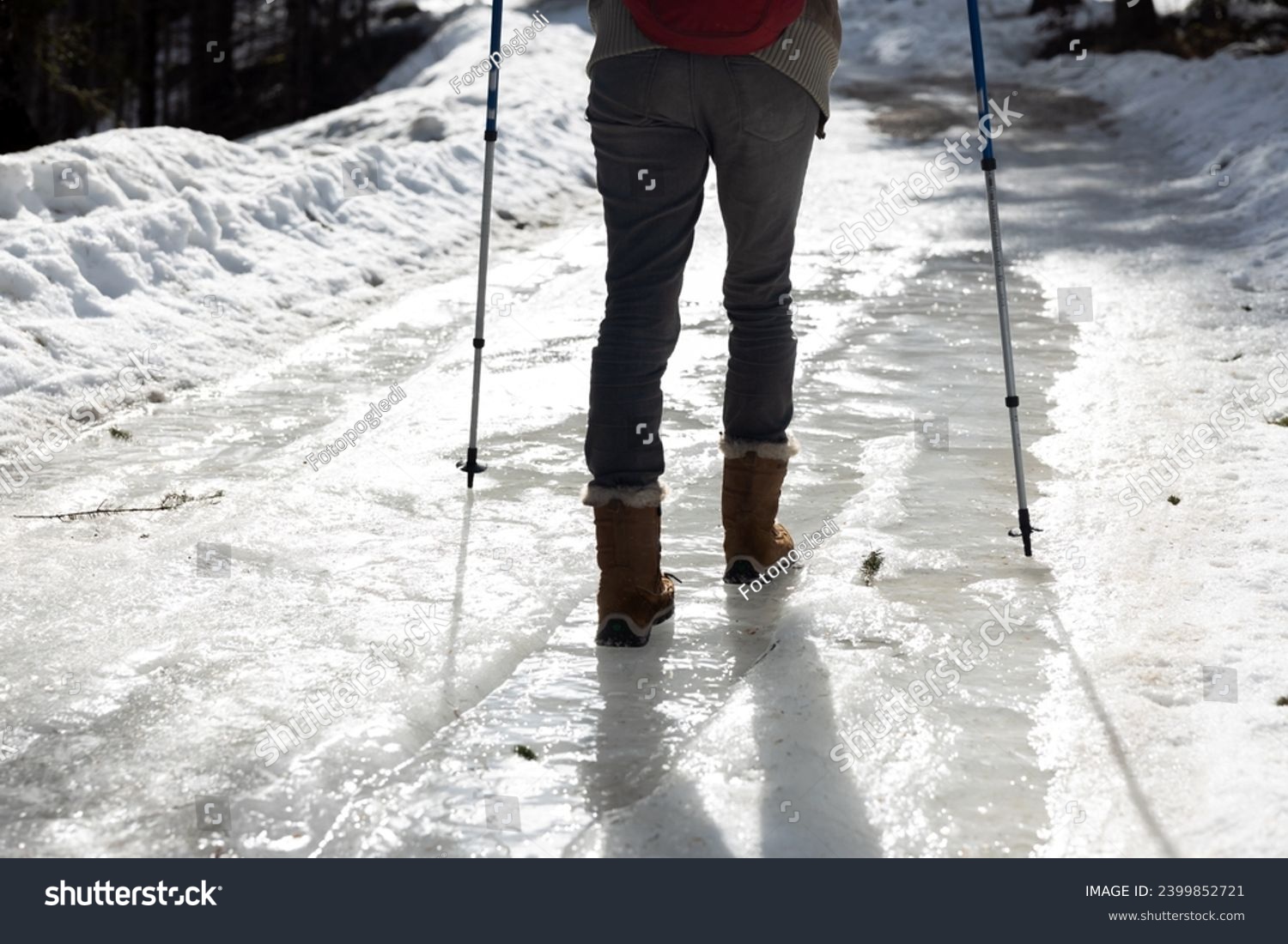 Woman Hiker Walking Carefully over part of Frozen Icy Road in Winter in Snowshoes and with help of Hiking Poles #2399852721