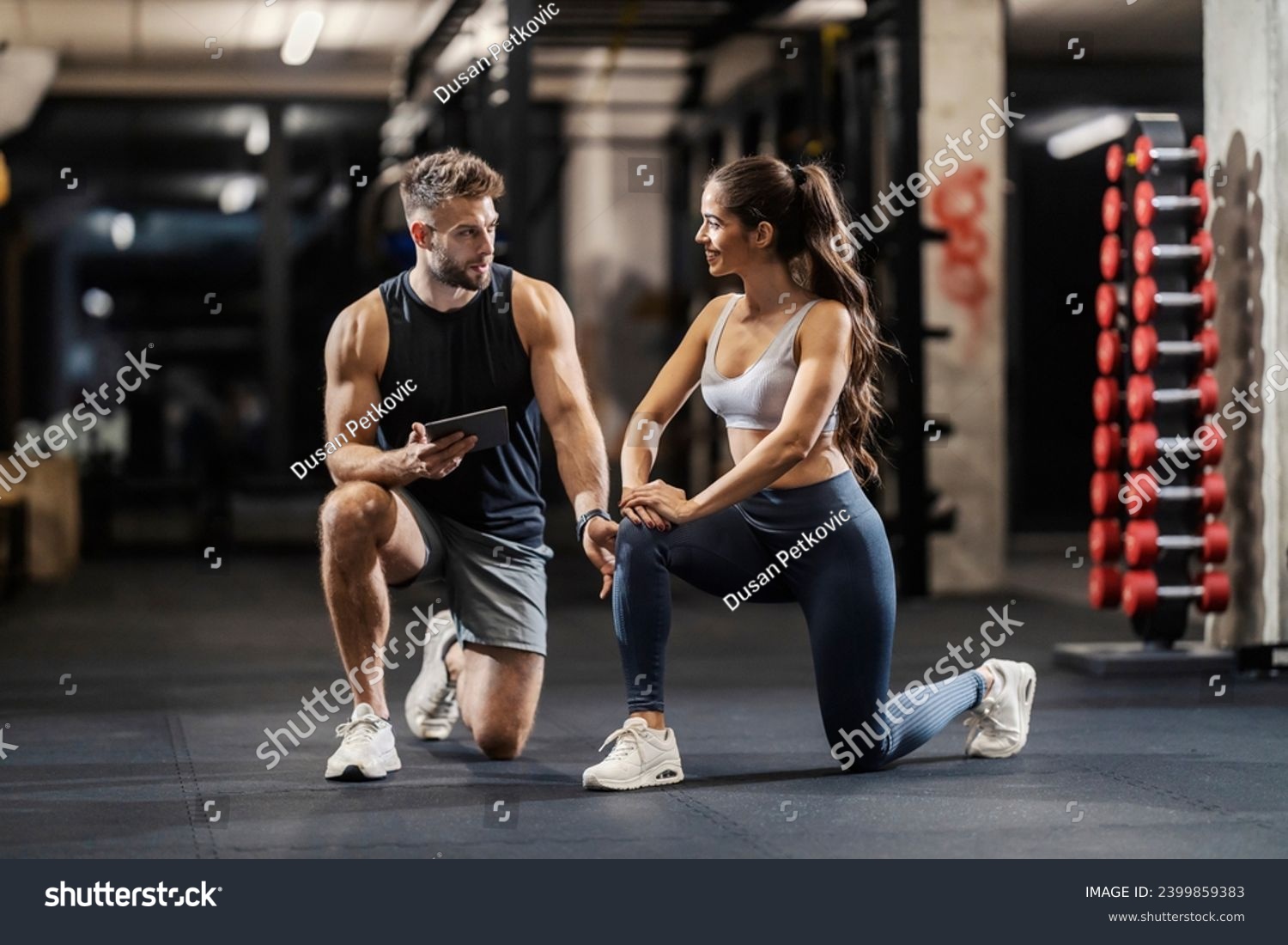 Personal trainer is showing a sportswoman how to do lunges correctly while kneeling in a gym. #2399859383