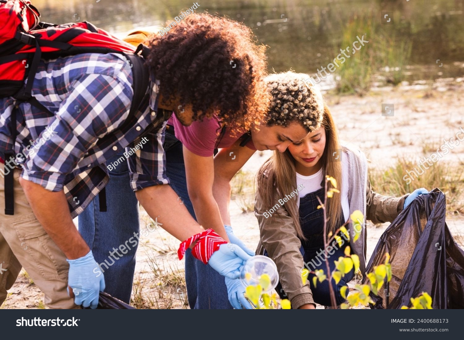 This image captures a moment of environmental stewardship, as a diverse group of volunteers engage in a community clean-up effort by a lake. The photograph features a Middle-Eastern man and a woman of #2400688173