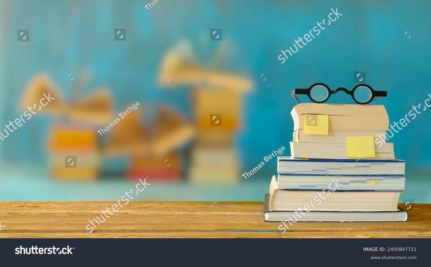 stack of books, bookmarks and spectacles, blurred open books in the background.Spring Book fair , inspiration,reading, education, literature concept, free copy space #2400847711
