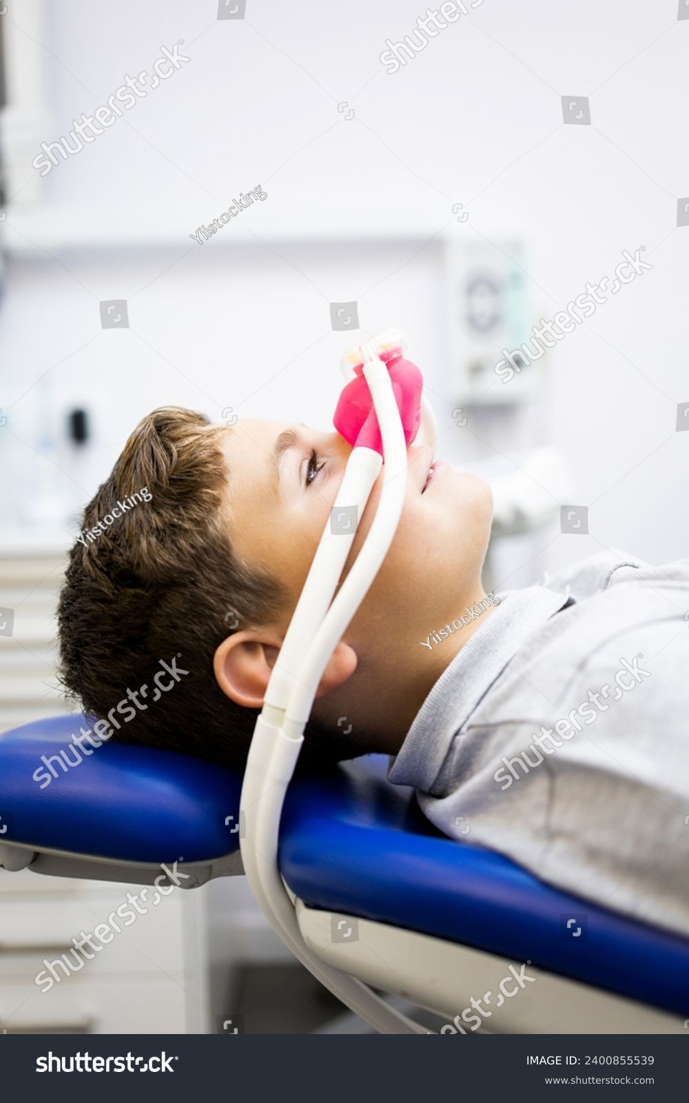 Fear of the dentist! Vertical photo of a little boy sits in a dentist's office wearing a nasal mask breathing nitrous oxide to relax. Concept of feeling relaxed with laughing gas. #2400855539
