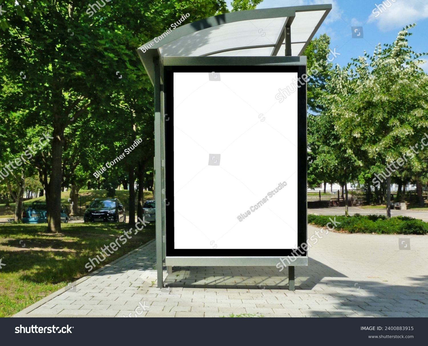 bus stop with blank white poster ad lightbox. bus shelter advertising concept. glass and aluminum. commercial poster space and display panel. green urban street. lush foliage. soft background #2400883915