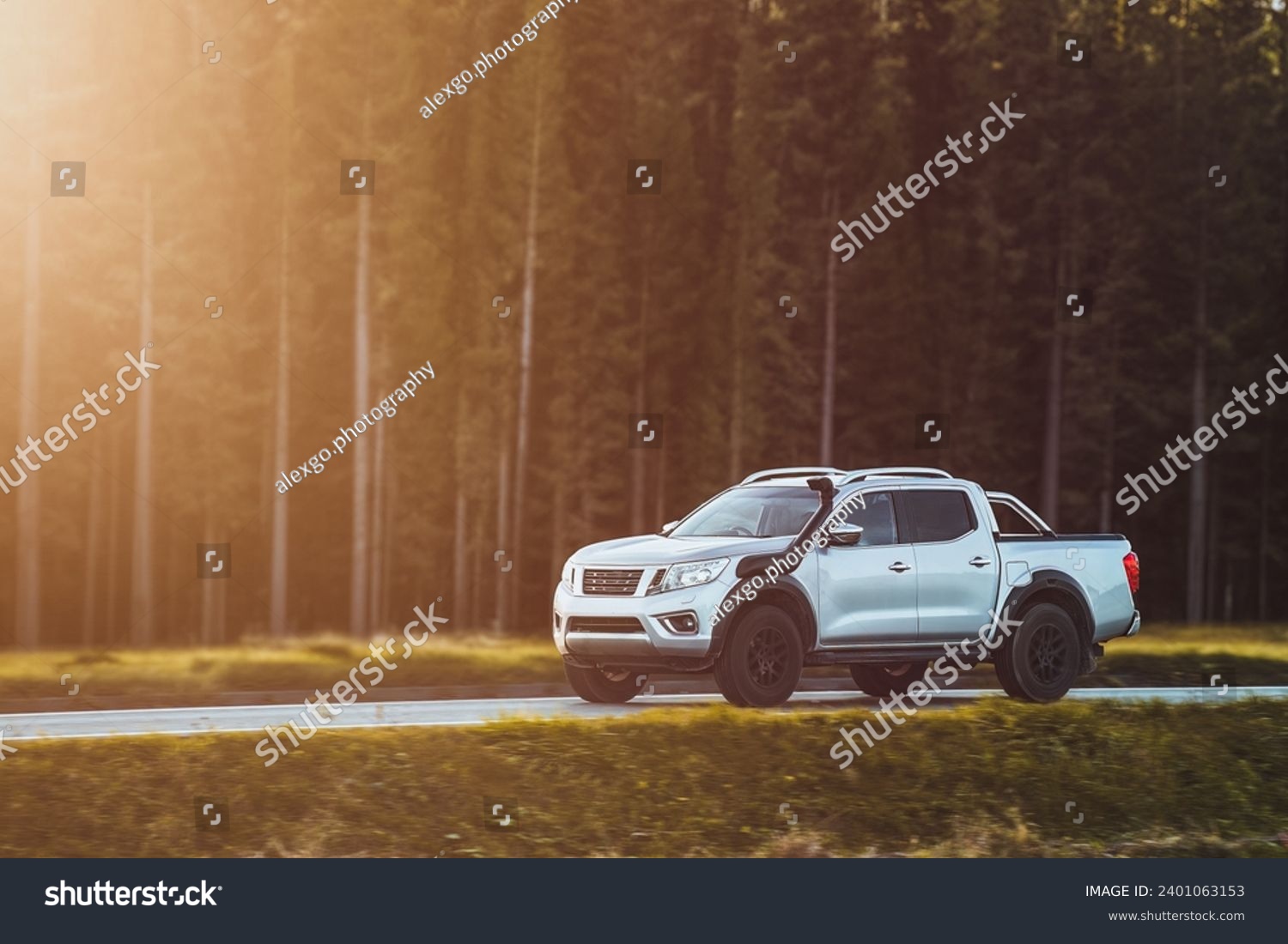 A pickup truck with a snorkel drives on a scenic road surrounded by mountains and trees. #2401063153