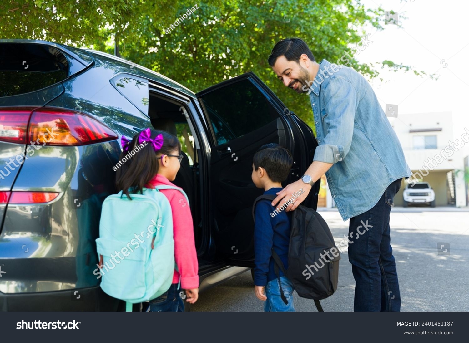 Cheerful father smiling while picking up his young children from elementary school and getting them into the car #2401451187