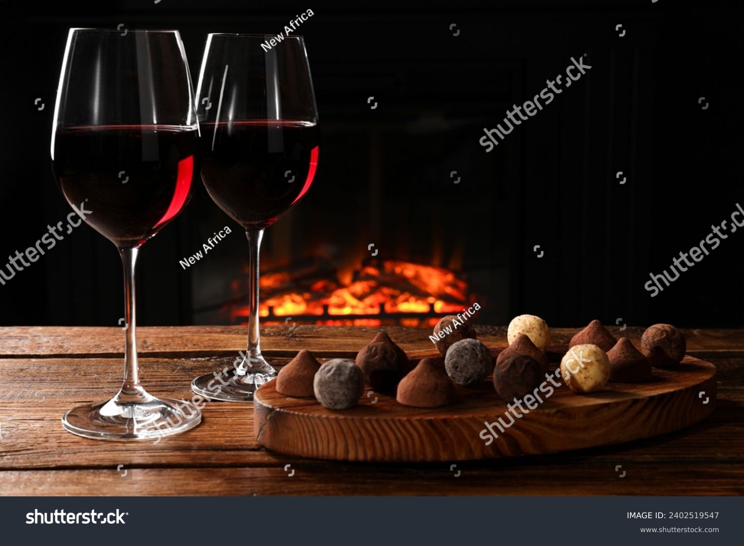 Red wine and chocolate truffles on wooden table against fireplace #2402519547