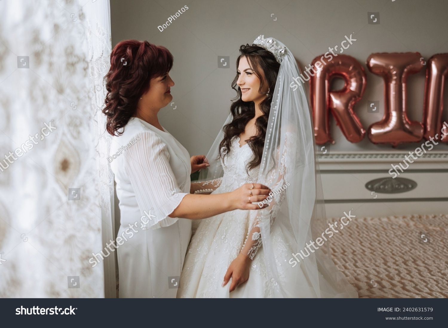A beautiful and happy mother and her daughter, the bride, are standing next to each other. The best day for parents. Tender moments at the wedding. #2402631579