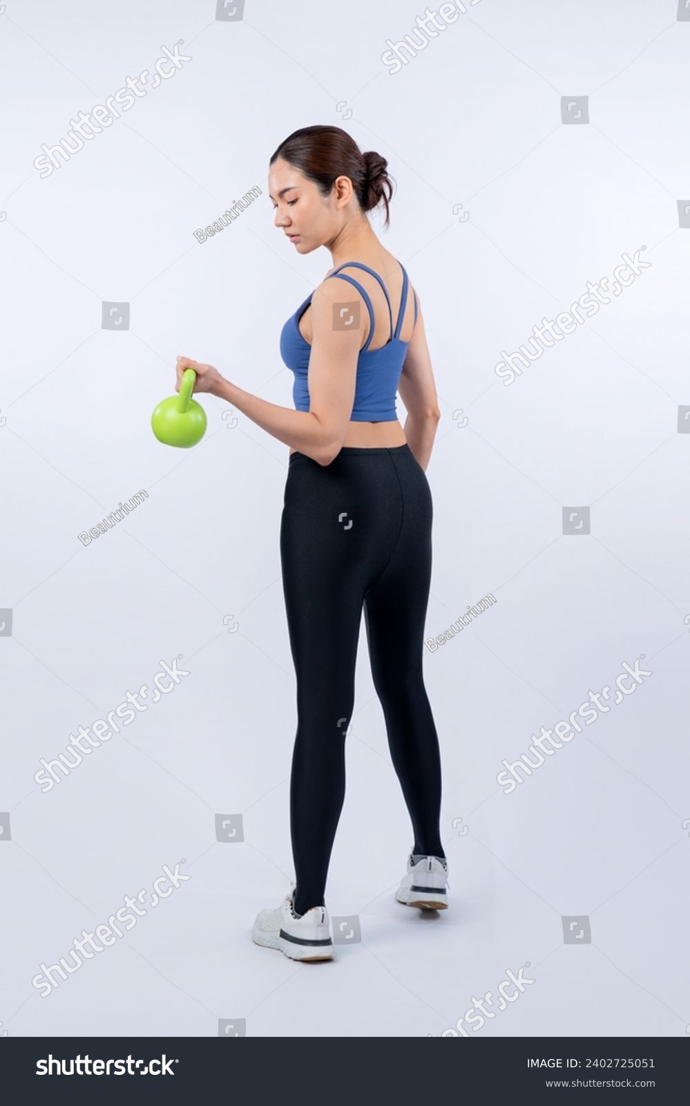 Vigorous energetic woman doing kettlebell weight lifting exercise on isolated background. Young athletic asian woman strength and endurance training session as body workout routine. #2402725051