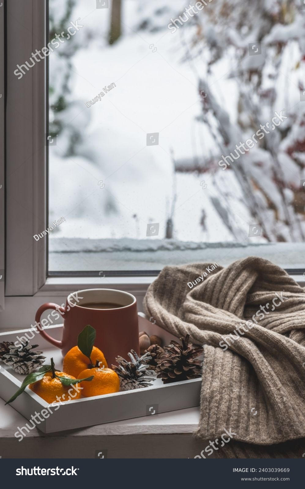 White tray with a mug of coffee and tangerines and a knitted scarf on a winter windowsill. Cozy winter composition. #2403039669