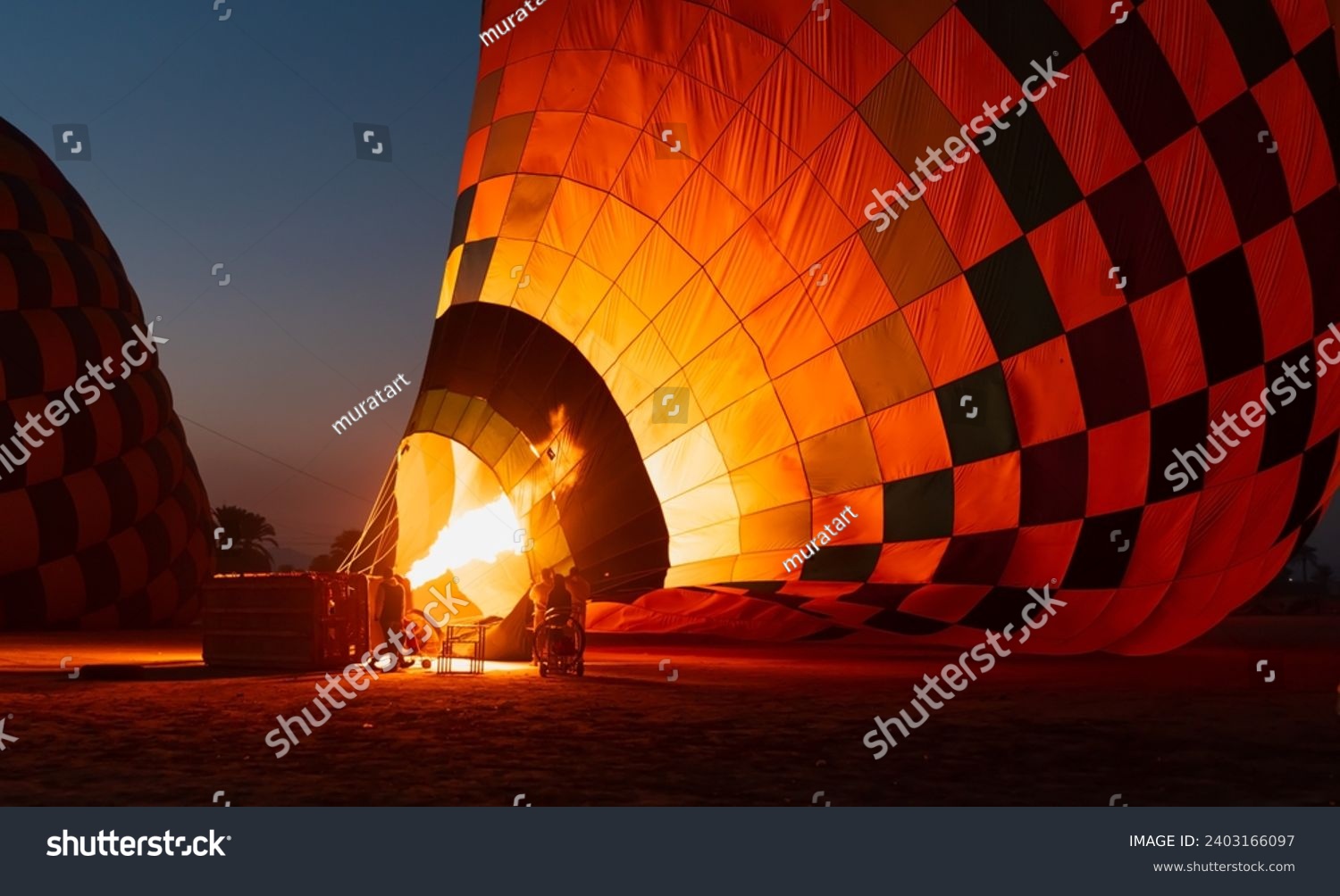 Hot air balloon is inflating before liftoff - Hatshepsut Temple at sunrise in Valley of the Kings and red cliffs western bank of Nile river- Luxor- Egypt #2403166097