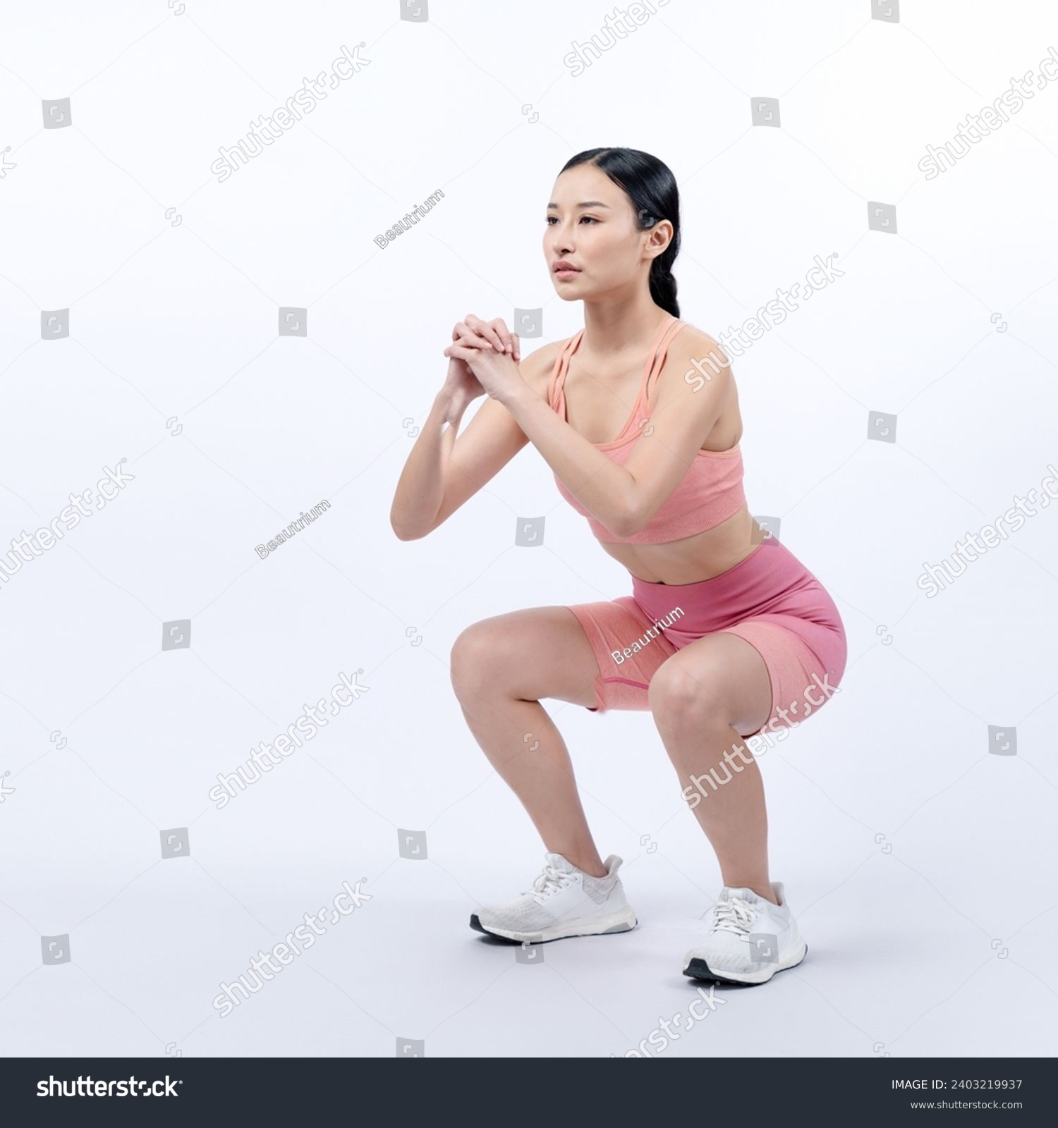 Vigorous energetic woman doing exercise. Young athletic asian woman strength and endurance training session as squat workout routine session. Full body studio shot on isolated background. #2403219937