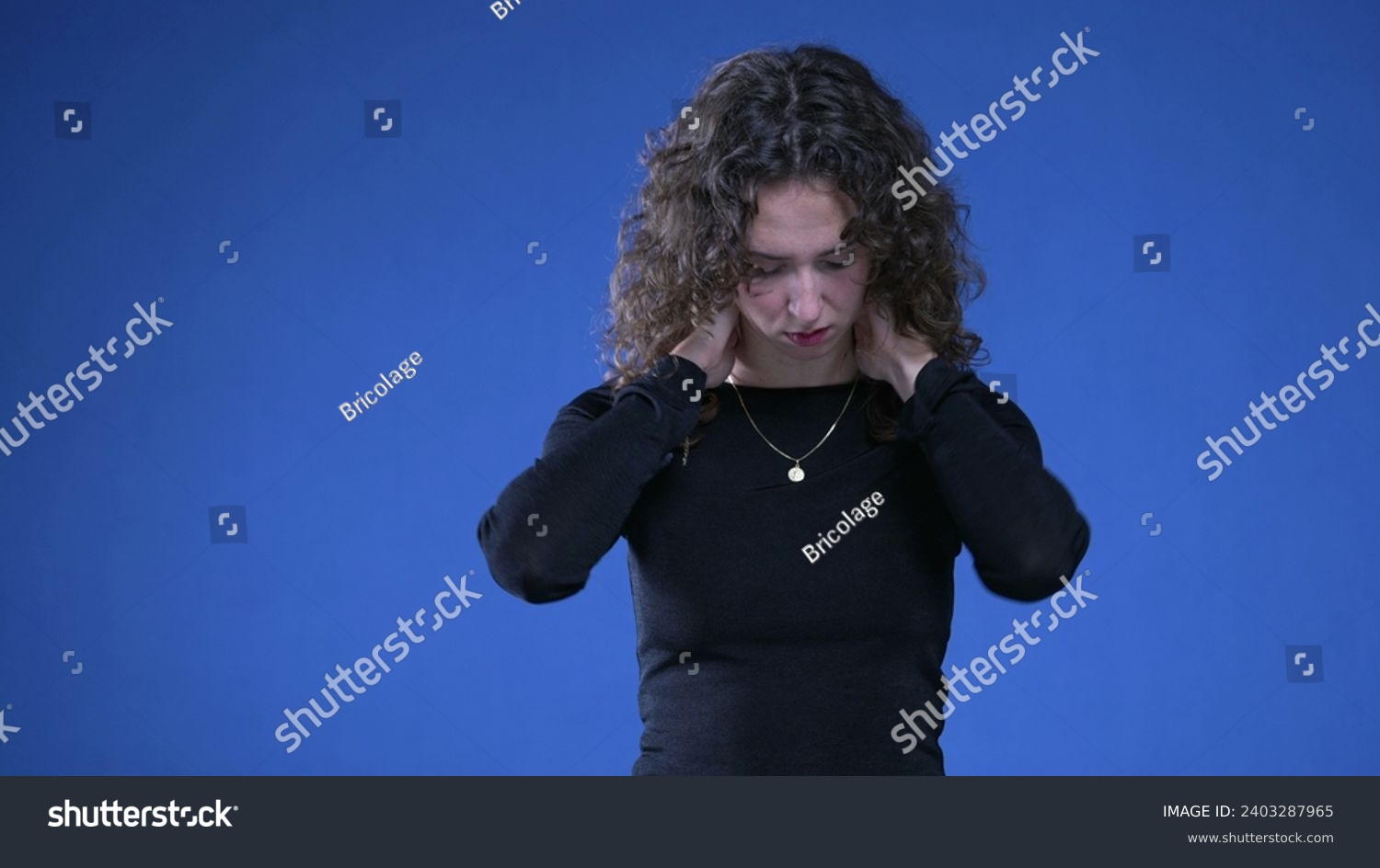 Stressed young woman rubbing neck trying to appease mental anguish while standing on blue background #2403287965