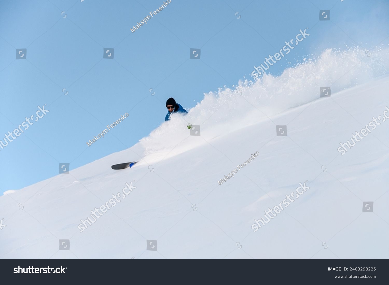 Male skier in a blue jacket goes down a snowy slope, so that he is almost invisible behind the powder snow #2403298225