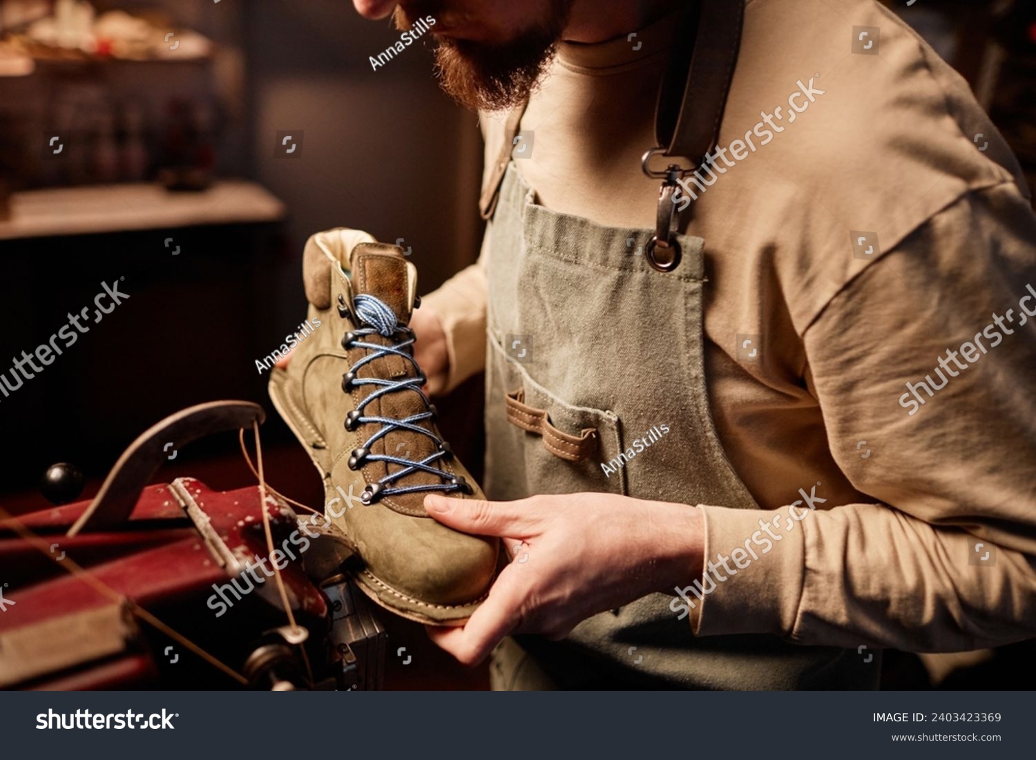 Young shoemaking master sewing upper part of boot workpiece together with sole #2403423369