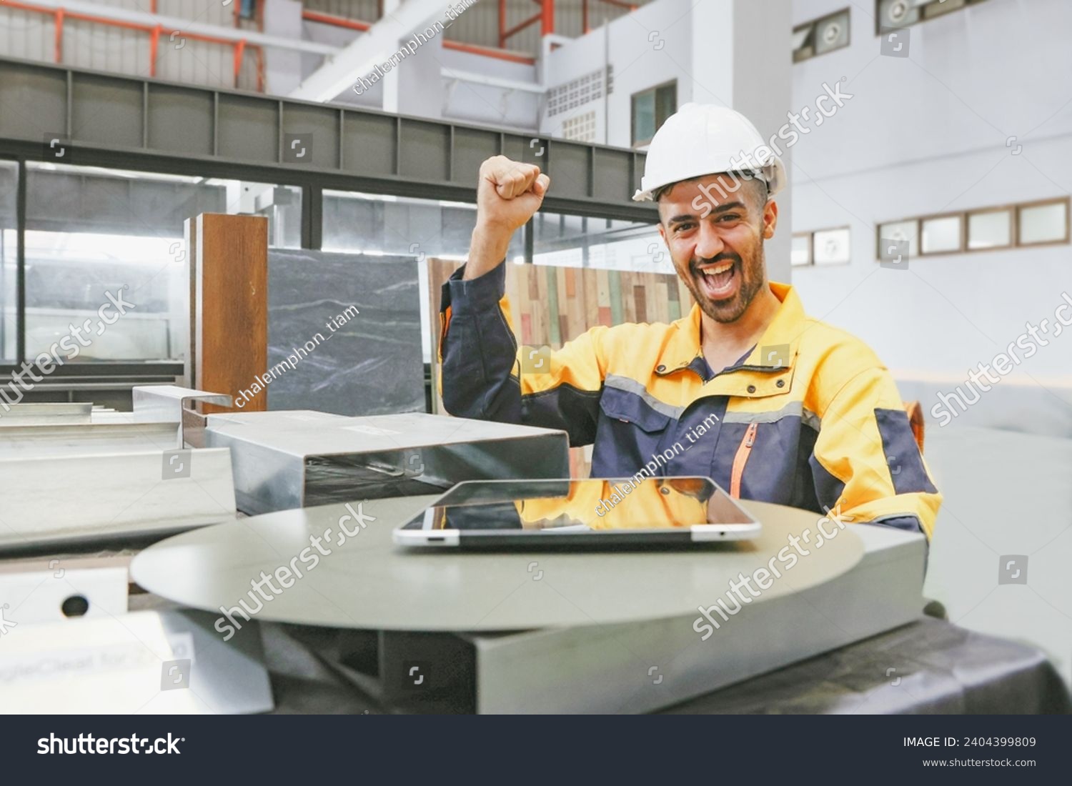 Male spanish worker technician with smile happy and having fun working in factory industrial company sitting with fist raised positive attitude strong and confident looking at camera factory office. #2404399809