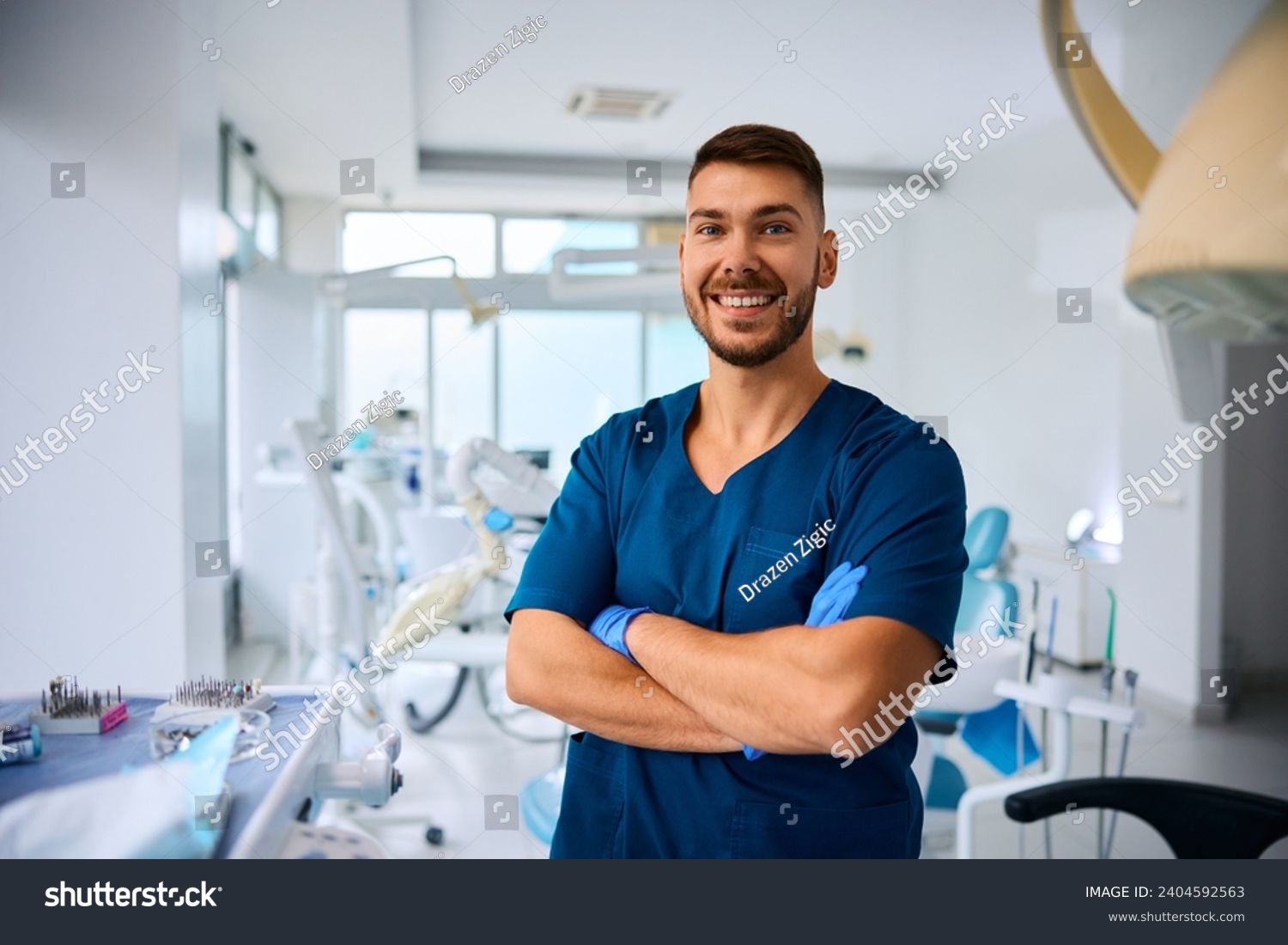 Happy dentist with arms crossed at dental clinic looking at camera. Copy space. #2404592563