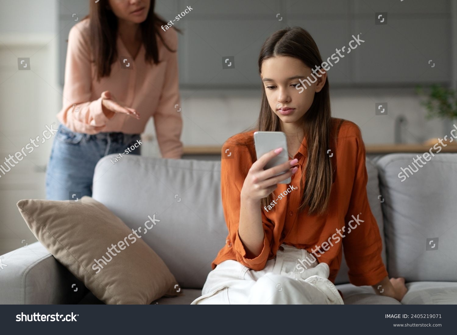 Angry mother shouting and arguing with teenage daughter over use of mobile phone, girl sitting on sofa at home, ignoring mom #2405219071
