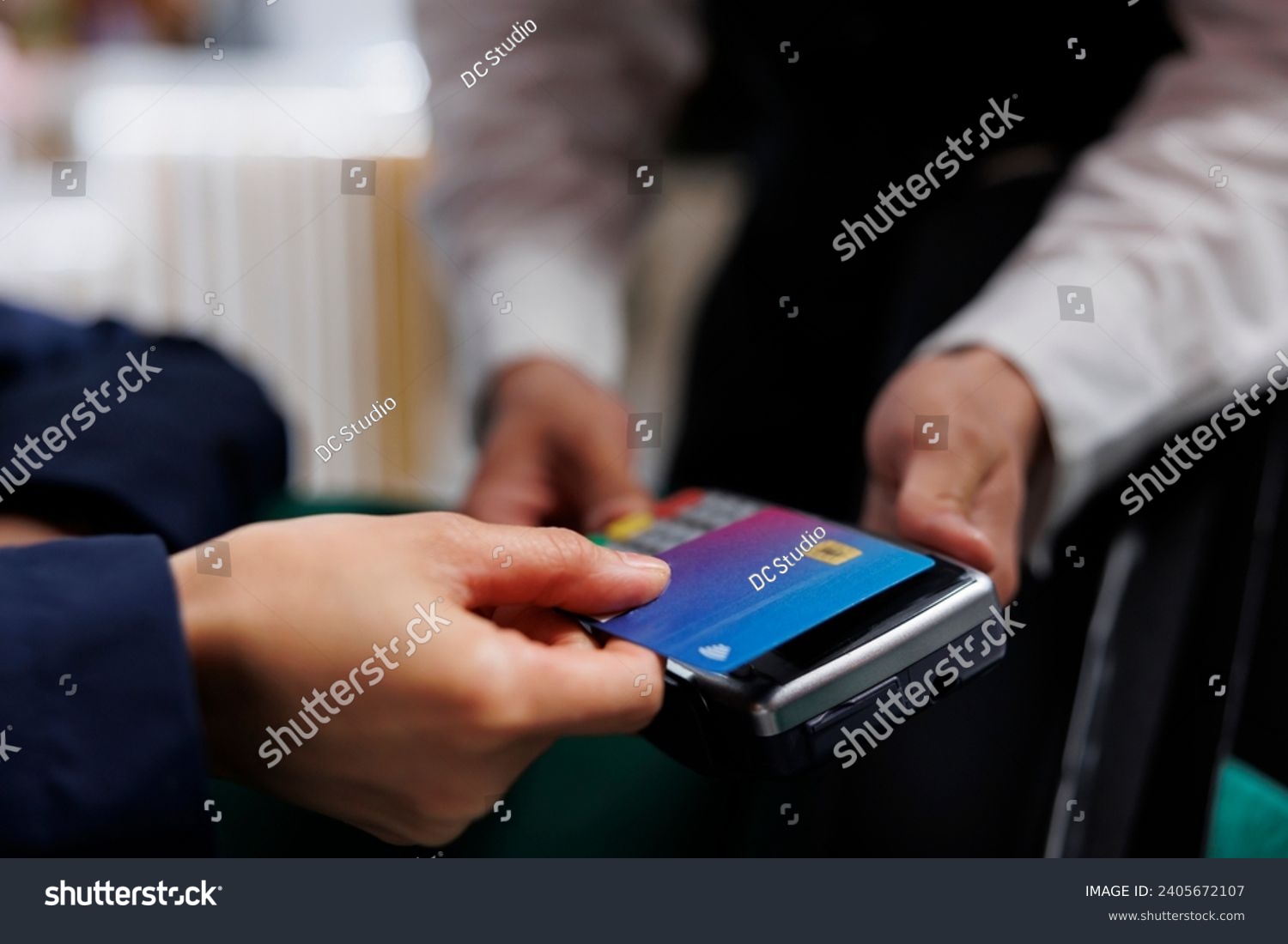 Close-up view of pair of hands grasping credit card and pos terminal at exclusive hotel reception. Detailed shot of person paying for reservation in lounge area of ski mountain resort. #2405672107