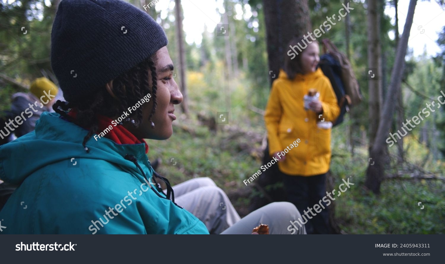 Group of travelers resting in camp after long walking trek in the mountains. Multiethnic young hikers talking, having snack in the forest during tourist trip or hike in autumn. Active leisure concept. #2405943311
