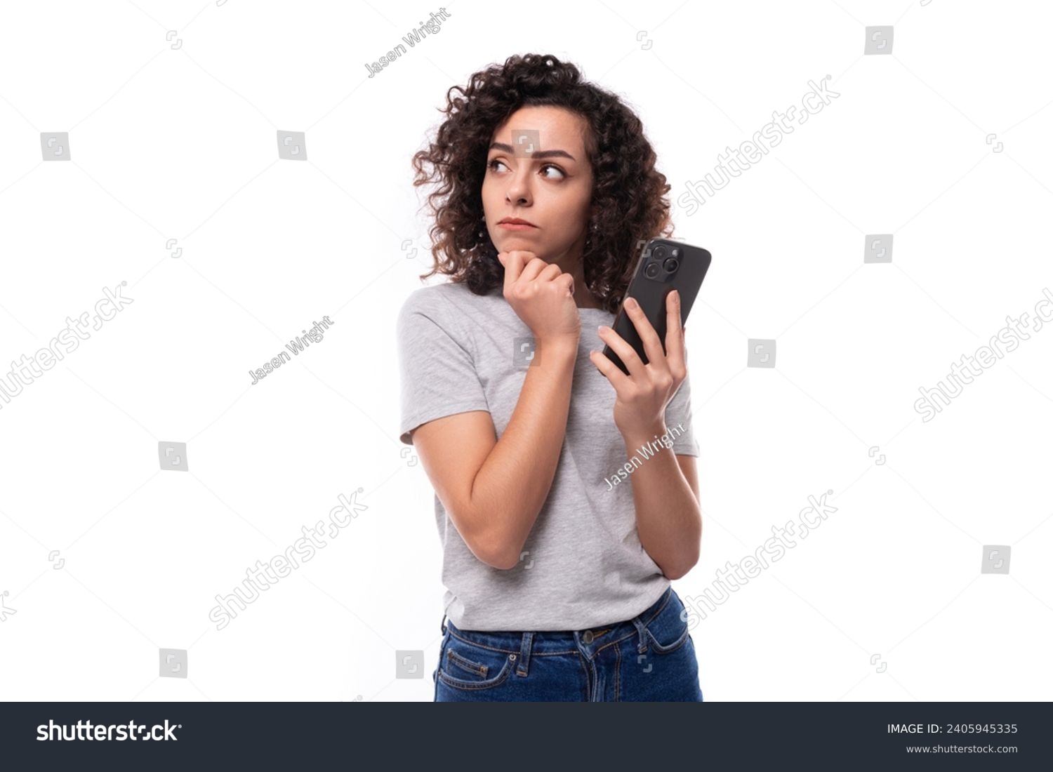 a young slender 30 year old caucasian woman with curly hair in a gray t-shirt uses instant messengers on a smartphone #2405945335