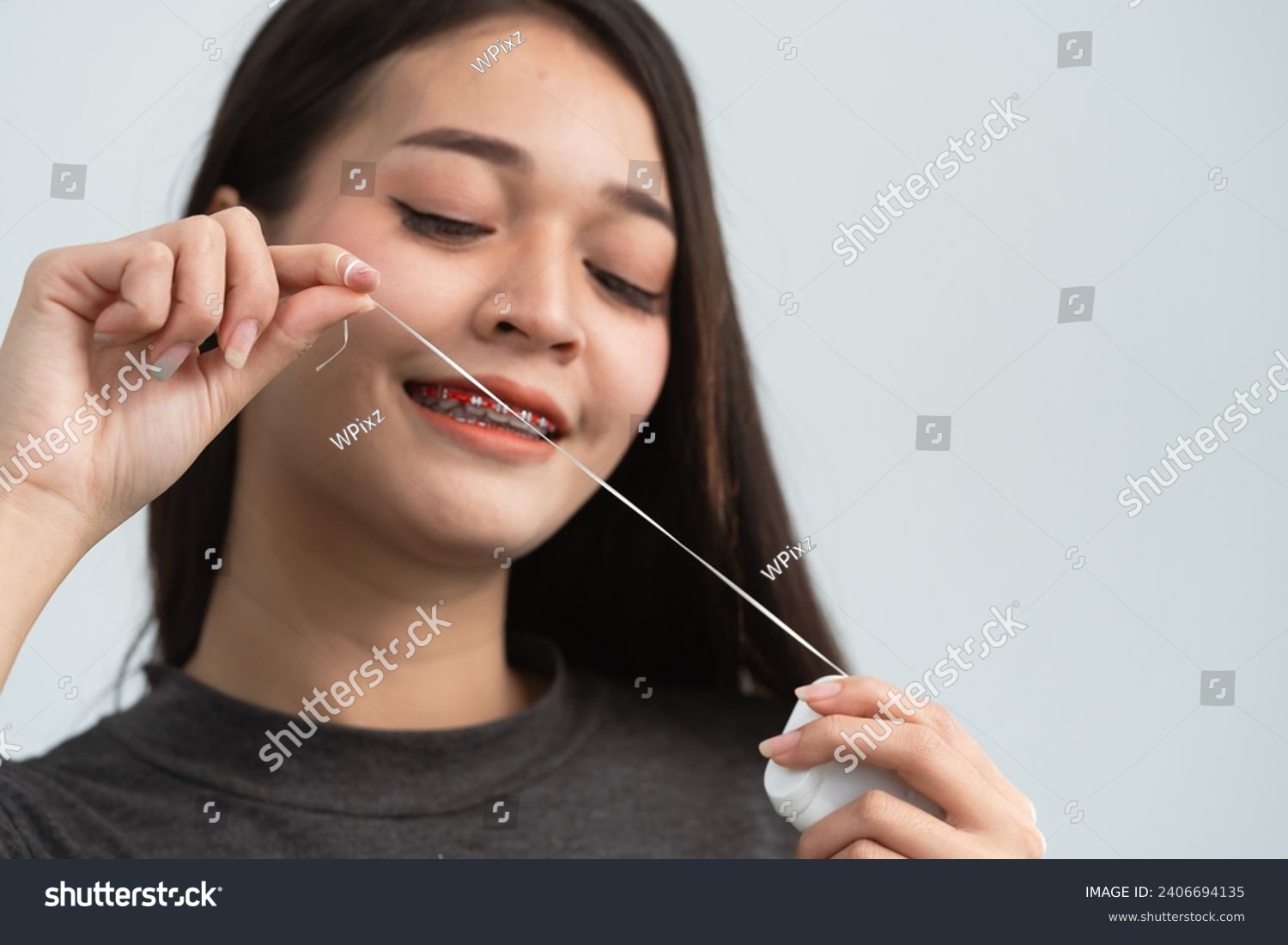 Asian woman braces using dental floss. Teeth braces on the white teeth of women to equalize the teeth. Bracket system in smiling mouth, close up photo teeth, macro shot, dentist health concept. #2406694135