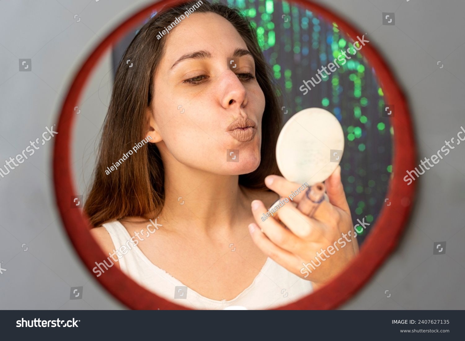 young woman in beauty and makeup center putting on makeup in front of a mirror and cell phone with a ring of light happy painting her lips and cheekbo #2407627135
