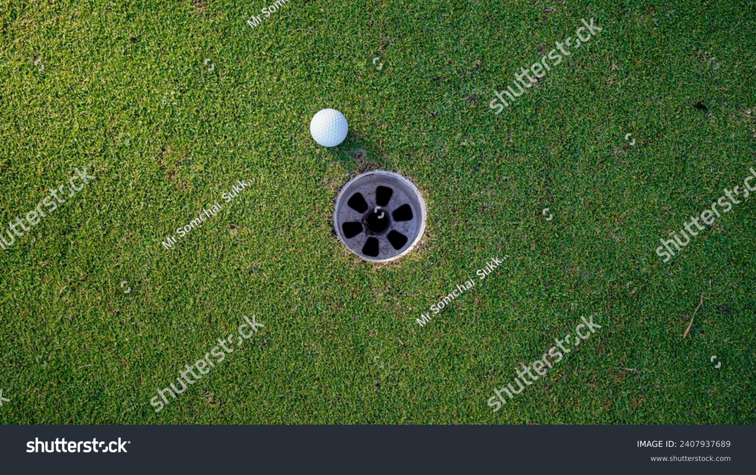 Selective focus. white golf ball in hole on green grass good for background with sunlight. golf ball beside the golf hole.                                #2407937689