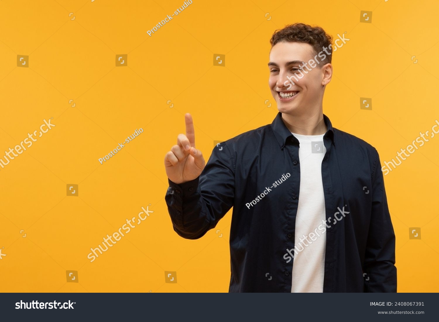 Positive caucasian guy touching invisible screen and smiling, copy space on yellow studio background. Happy young man pushing button on virtual display, interacting with touchscreen #2408067391