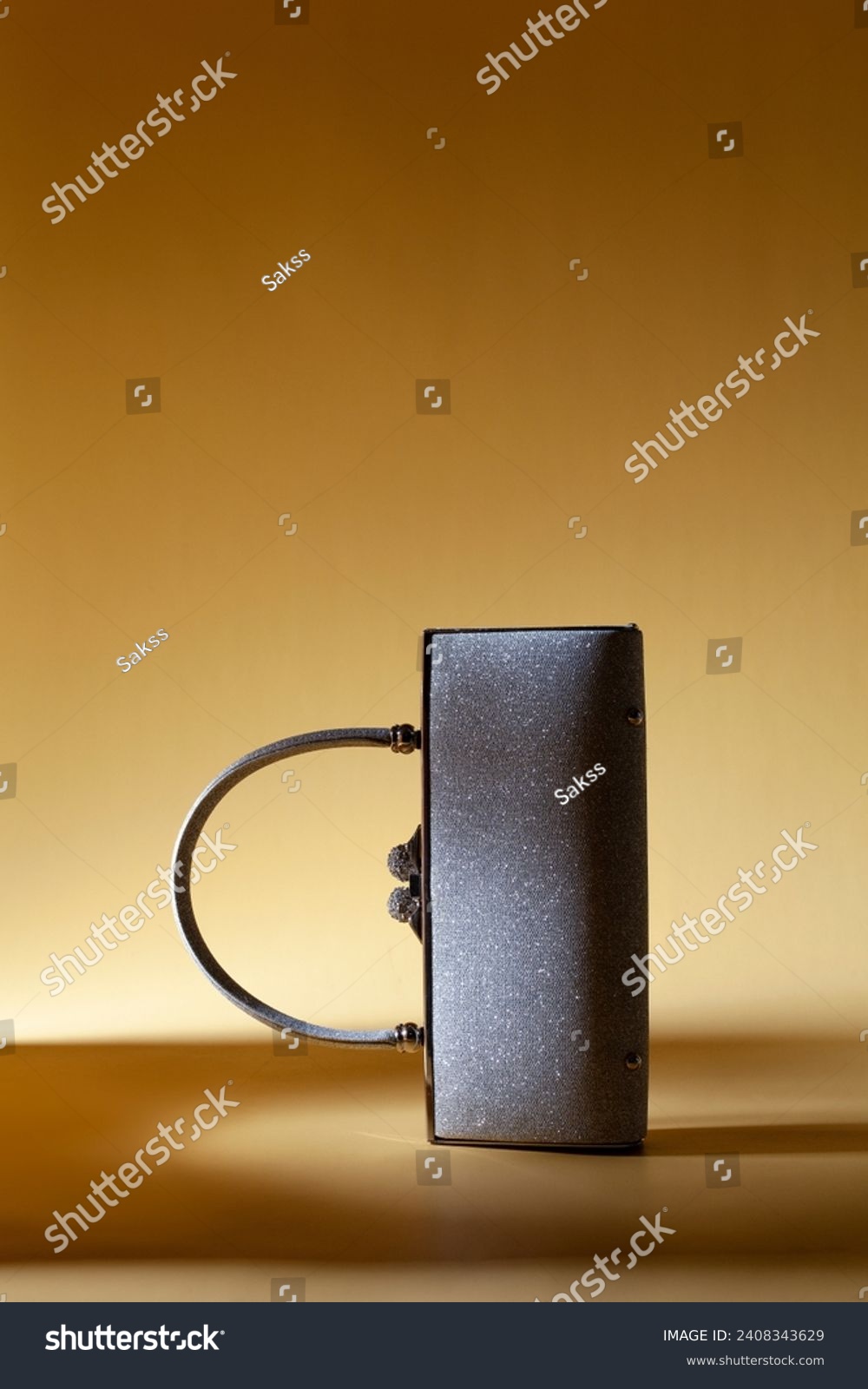 Shiny sparkling silver like woman purse with handle on a yellow background. Creative studio shoot  #2408343629