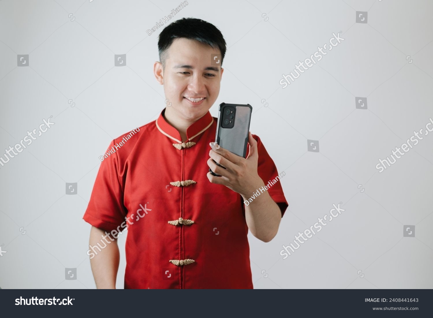 Smile face of Asian man wearing Chinese traditional cloth or Cheongsam while looking at his smartphone on white background #2408441643