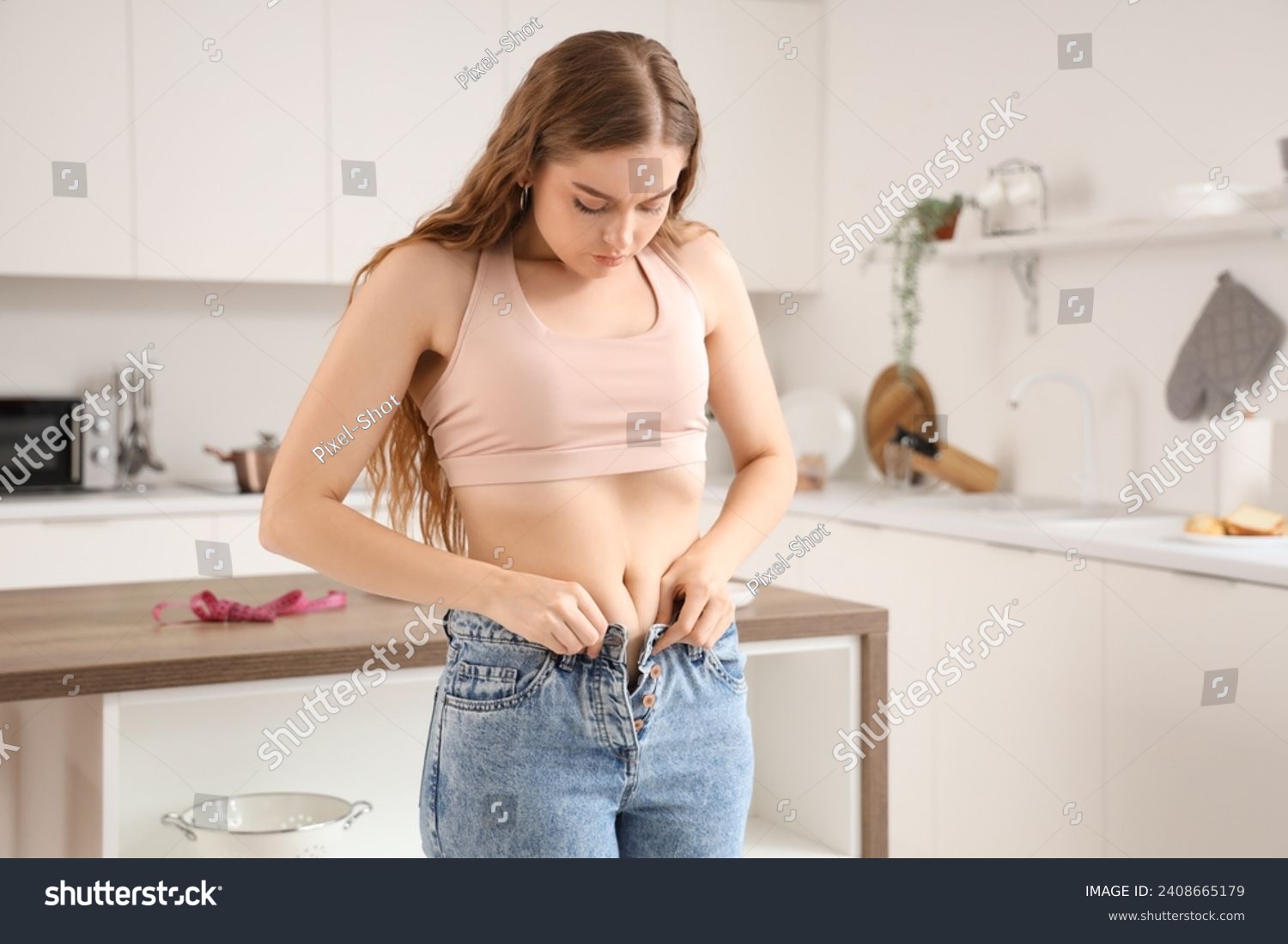 Young woman in tight jeans at home. Weight gain concept #2408665179