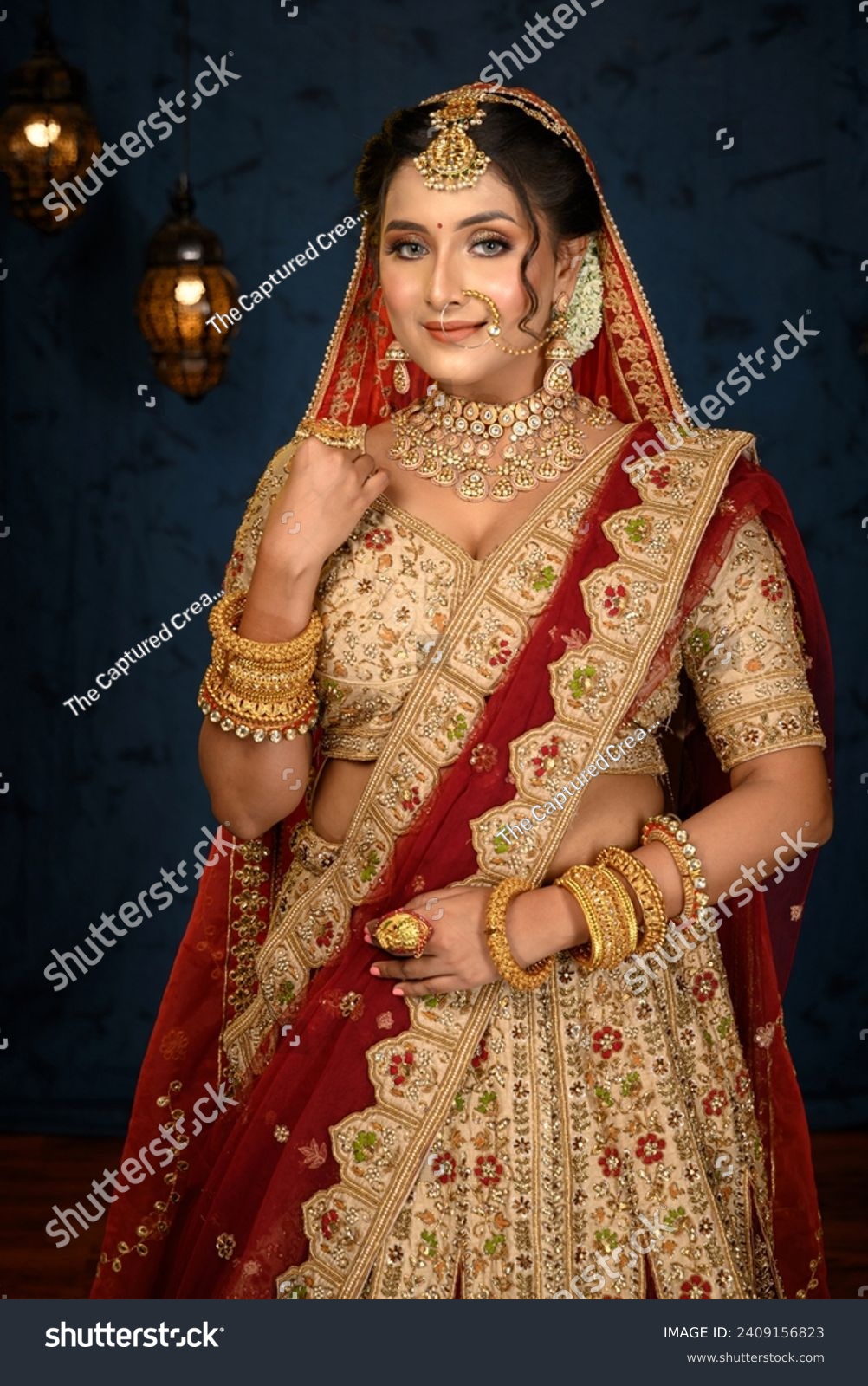 Stunning Indian bride dressed in traditional bridal lehenga with heavy gold jewellery and veil posing fashionable in studio lighting. Wedding fashion and lifestyle. #2409156823