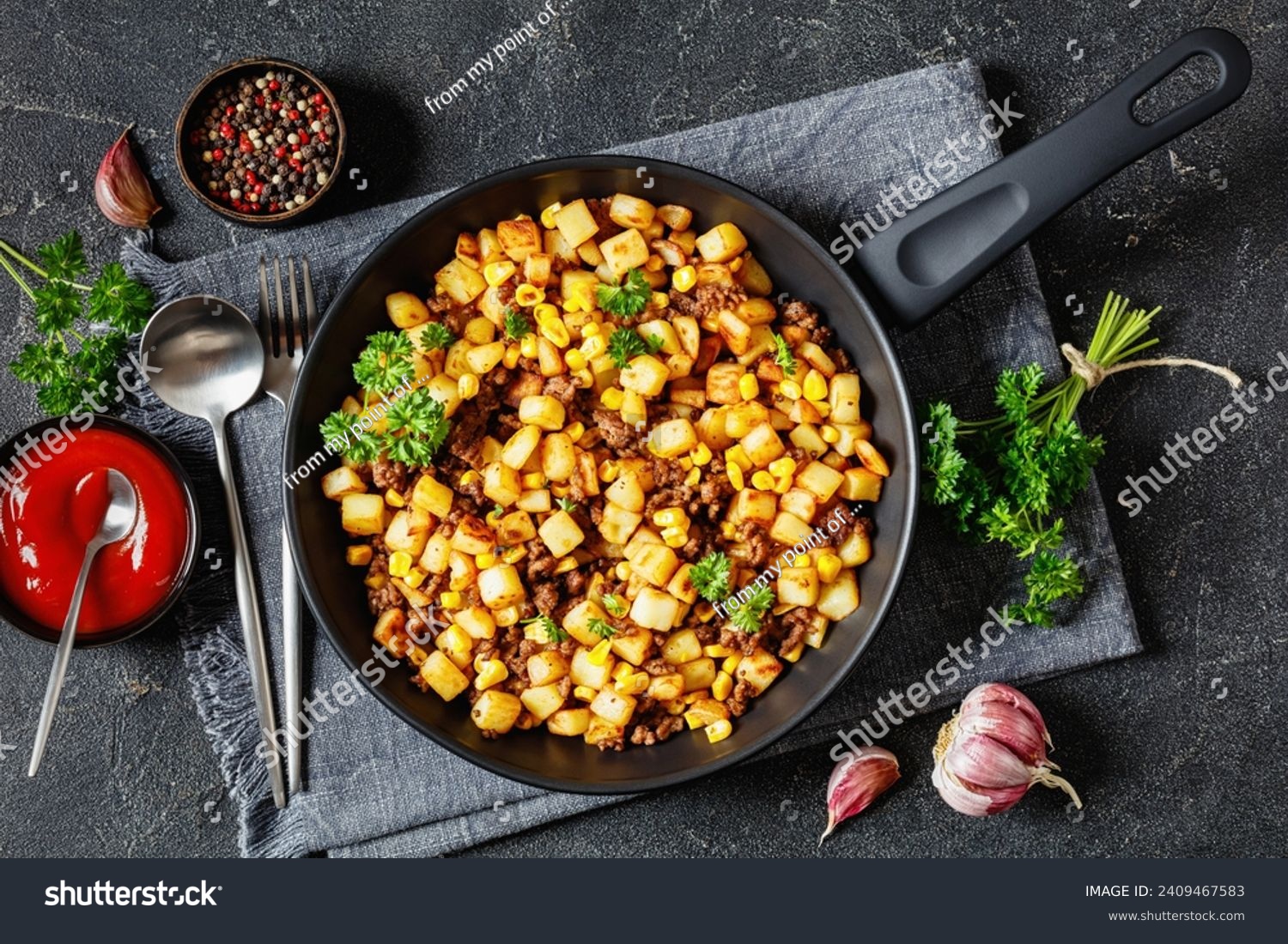 Beef Hash with roasted corn, garlic and parsley on a skillet on concrete table with ketchup, fork and spoon, horizontal view from above, flat lay #2409467583