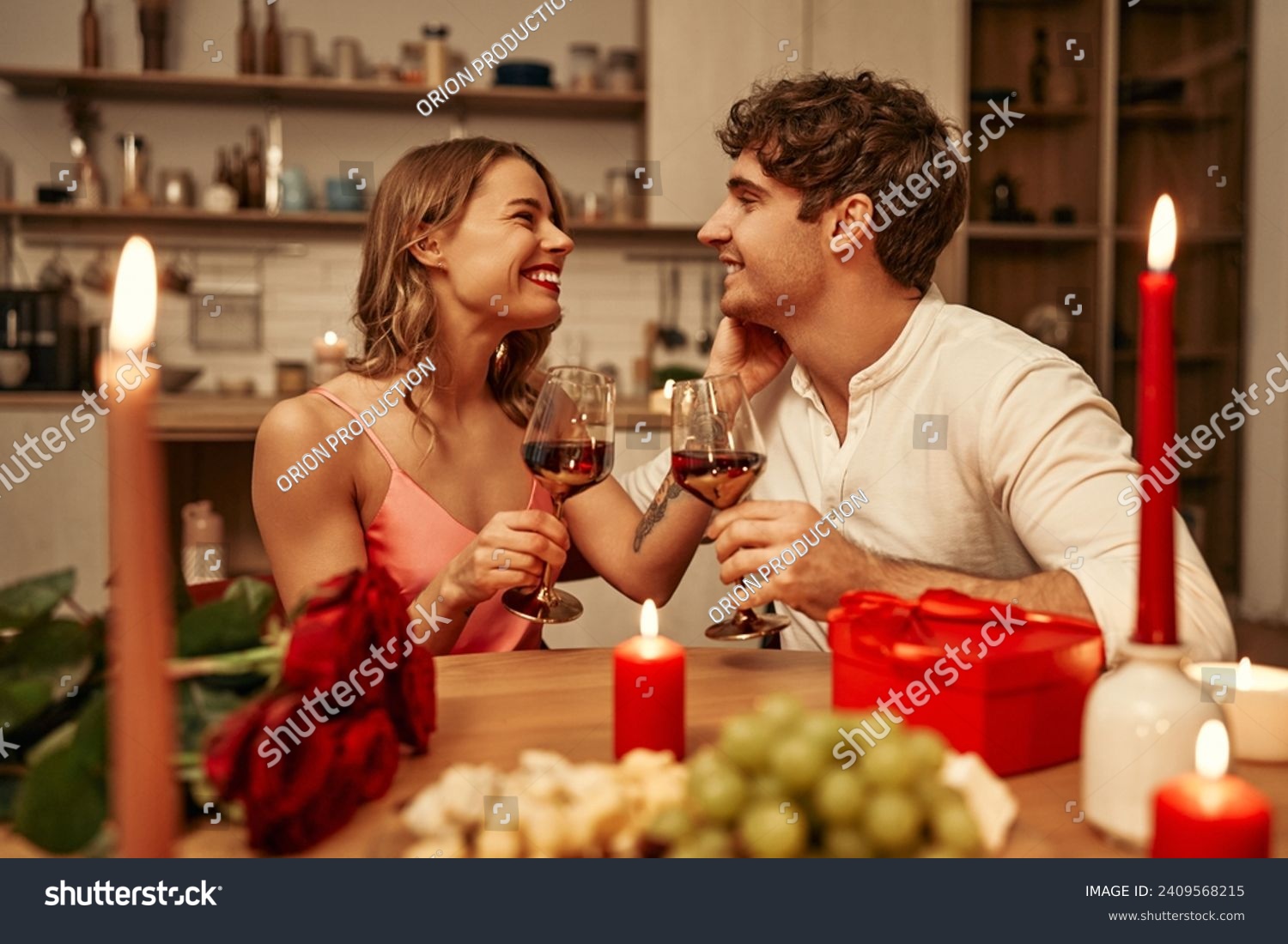 Happy Valentine's Day. A young couple in love with glasses of wine by candlelight sitting in the kitchen at the table, romantically spending the evening together. #2409568215