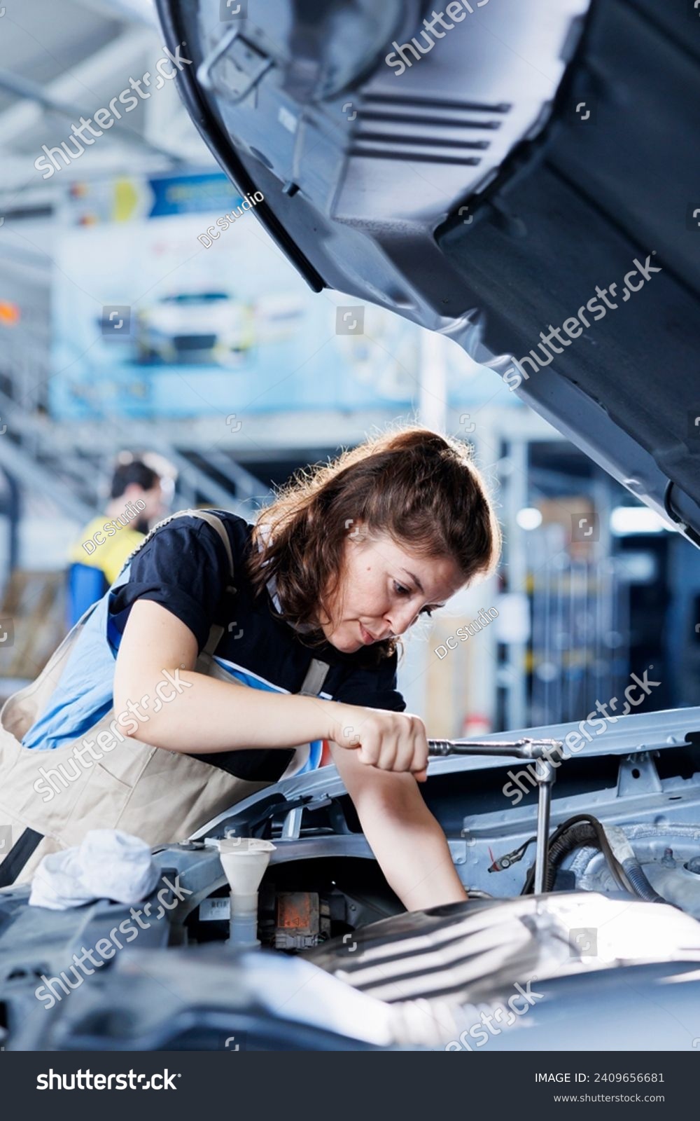 Technician in car service uses torque wrench to tighten bolts after replacing engine. Diligent auto repair shop employee uses professional tools to fix customer automobile #2409656681