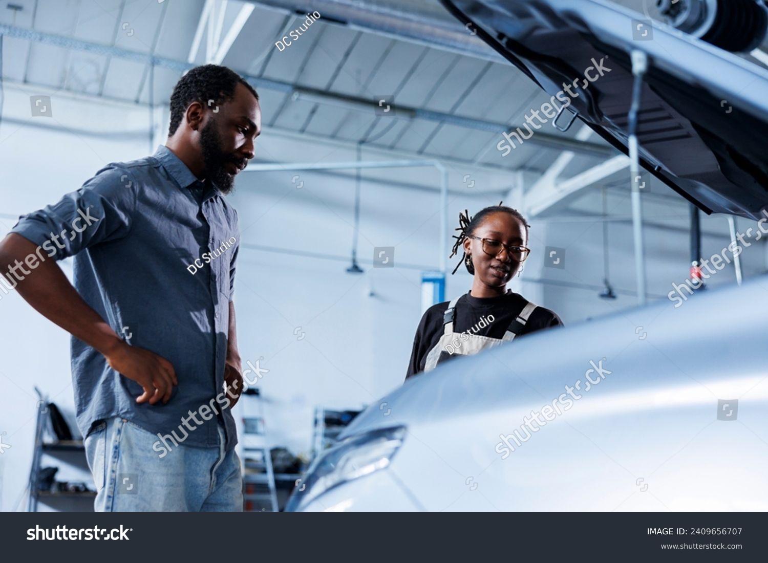 Mechanic at auto repair shop conducts annual vehicle checkup, informing customer about needed steering mechanism replacement. Competent garage worker talks with customer after finishing car inspection #2409656707