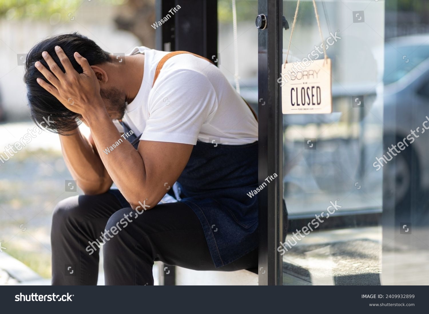 Young man running a small start-up business sits at the entrance looking absent-minded. Entrepreneurs starting small startups are stressed out and forced to close shop due to the economic crisis. #2409932899