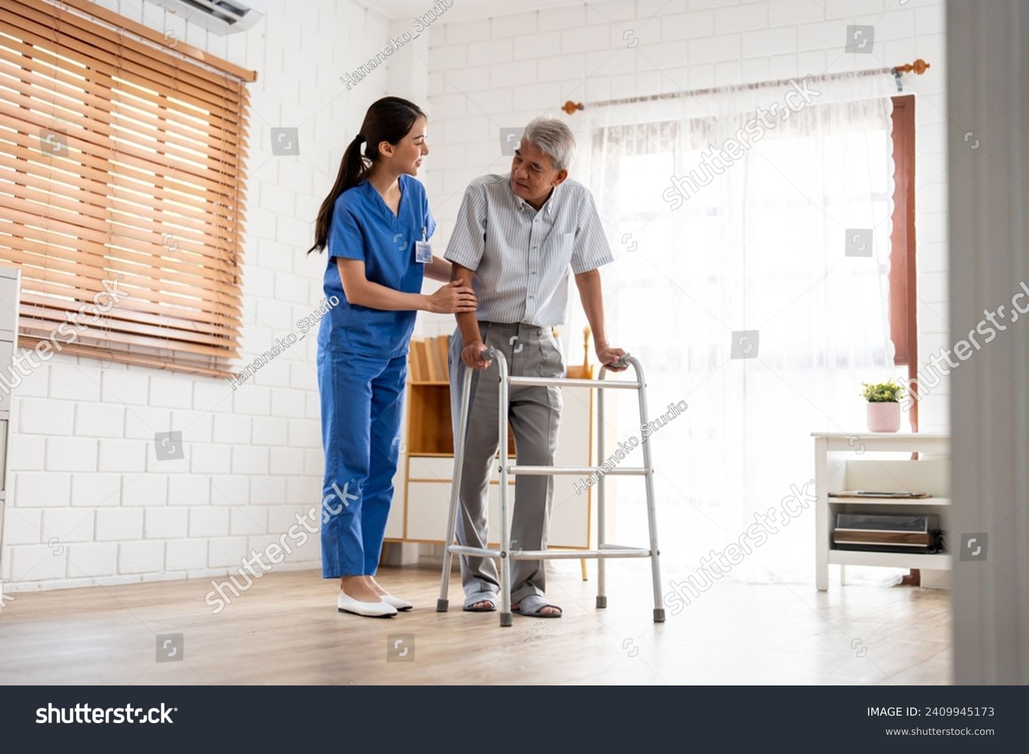Asian senior elderly man patient doing physical therapy with caregiver. Attractive specialist carer women help and support older mature male practice walking slowly with walker at nursing home care. #2409945173
