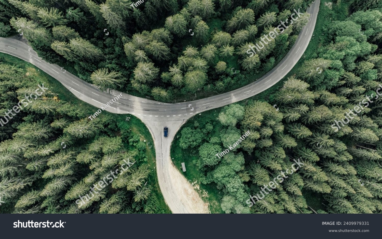 Birds eye view onto a car stopping at a crossing on a curvy road through the forest #2409979331