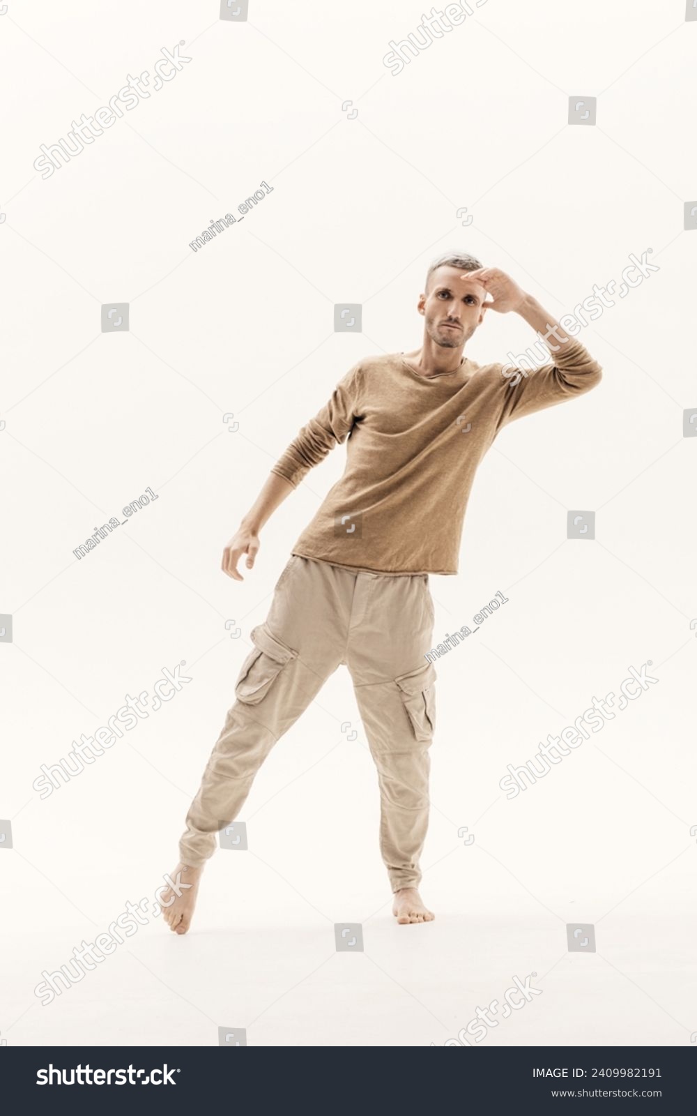 A young man in a beige jumper and cargo pants on a white background. #2409982191